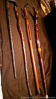 Four handcarved wooden canes laid out on a dark fabric background showing different styles and textures.