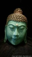 Front view of the handcarved Buddha statue mask showing green and gold paint with serene facial features.
