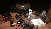 Overview of the lot showing cameras, camcorder, cables, remote control, carrying bag, and memory card reader.
