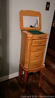 Front view of the wooden jewelry chest with the top lid open showing the mirror and green felt compartments.