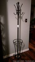 Full view of the wrought iron upright coat and umbrella hanger showing the structure and base stand.