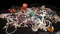 Pile of assorted costume necklaces showing pearl beads, colored beads, metal chains, and various pendants.