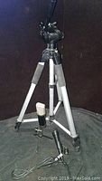 Full view of aluminum tripod including legs with foam grips and adjustable head, standing on black surface.