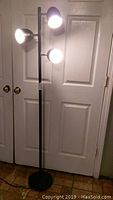 Front view of the 3 shade floor lamp showing three lit shades on black pole with round weighted base.