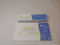 Box with Glister toothpaste on top and box with 4 toothbrushes below, product names and details visible.
