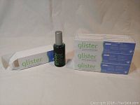 Photo showing one opened tube of Glisten multi-action fluoride toothpaste in white box, black-green oral rinse bottle, and five additional toothpaste boxes stacked horizontally.