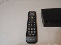 Dreamlink black streaming device partially visible with one remote control laying flat beside it on white surface