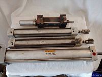 Four assorted pneumatic cylinders on white cloth, varying sizes with metal fitting ends.
