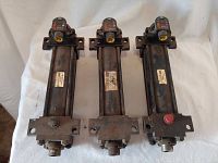 Three used Parker pneumatic cylinders shown side by side with visible mounting brackets and fittings, slight surface rust and wear.