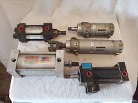 Overview of five assorted pneumatic cylinders arranged on white cloth surface showing size and designs