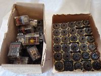 Two cardboard boxes filled with various electrical relays and relay sockets.