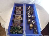 Two blue bins containing multiple Allen Bradley metal push-button and selector switch assemblies along with plastic caps in various colors and sizes.