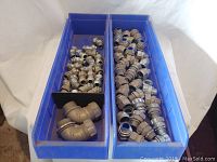 Two blue bins filled with metal pipe fittings, showing elbows and straight connectors.