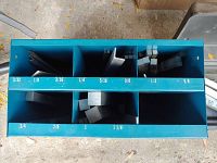 Top-down view of blue metal shelf organizer holding multiple keystock steel bars separated by size compartments labeled from 3/32 to 1 1/4 inches.