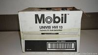 White cardboard box labeled Mobil UNIVIS HVI 13, hydraulic oil. Box designed for 12 one-liter bottles, partially opened with 11 bottles inside visible.