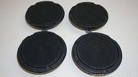 Four round black Ford Mustang OEM premium door speakers with protective mesh covers, backs facing down, front grilles facing up, showing one pair of speakers flipped open showing grill covers.
