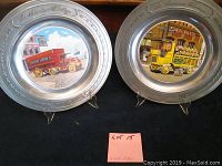 Pair of cast pewter plates with ceramic tile inserts showing colorful vintage Mack trucks, displayed upright on stands