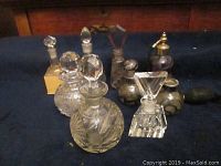 Photo showing nine vintage perfume bottles, various shapes and sizes, mostly clear glass or crystal with faceted stoppers