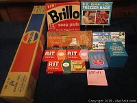 Overview of multiple vintage paper boxes containing various household and craft products including Brillo soap pads, freezer bags, clothes pegs, canning jar lids, tint and dye boxes, drinking straws, and birthday candles