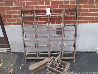 Wooden wool spool holder with slots holding 20 wooden spools, standing against a brick wall with the pants iron board and loom placed in front.