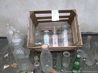 Wood crate filled with various vintage glass bottles including Mason jars, dairy bottles, and pop bottles arranged on and beside the crate.