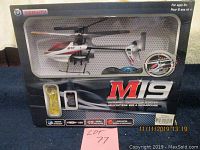 View of helicopter in original packaging with remote and USB charging cable visible, box shows wear.