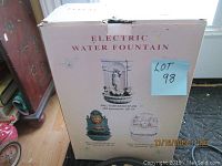 Photo of the unopened box showing electric water fountain model WF-295 with image of female figure and shell design.