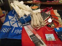 Photo showing blue and white Canadian flag with 1867 and 1967 markings, bundles of white twine, and several folded flags including USA vinyl flag.