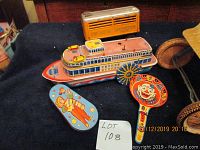 Photo showing 12-inch tin litho toy boat, two colorful lithographed tin maracas with clown designs on black cloth background.