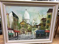 Full view of the framed and signed oil painting depicting Paris, showing buildings and the dome of the basilica.