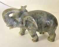 Side view of solid marble elephant figurine showing carved details and the curled trunk.