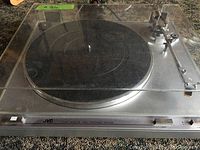 Front view of vintage JVC turntable with clear dust cover showing black platter mat and speed control slider on front edge.