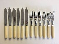 Set of six vintage knives and six forks arranged side by side showing full length with ivory-colored handles and shiny metal blades and tines.