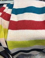 Close-up of wool blanket showing bold colored stripes of teal, red, yellow, and black on cream background.