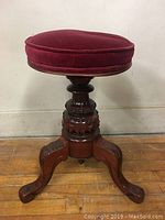 Full side view of the piano stool showing the padded seat and carved wooden legs.