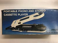 Photo of original cardboard package showing the full device with foldable handle, portable phono turntable, and cassette player.