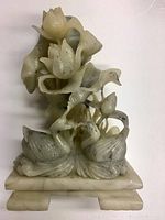 Front view of the marble sculpture showing two birds and curling flower buds above on a rectangular base.