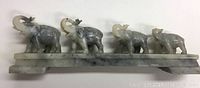 Full view of four elephants carved in marble on a rectangular base measuring 10.5 inches long.