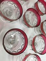 Overhead view of eight vintage cranberry flash dishes showing clear glass with cranberry red flash rim detailing and ornate inner pattern.