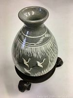 Full view of the gray pottery vase on metal stand showing bird and linear pattern decoration.