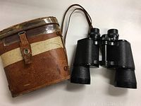 Binoculars and carrying case shown side by side on white surface to display overall condition and appearance.