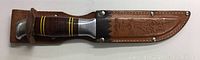 Full view of hunting knife sheathed in a brown leather case embossed with deer and floral pattern, reinforced with metal rivets.