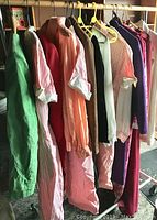 Full rack of vintage clothing showing various dresses, jackets, blouses, and pants hung on hangers, colorful with reds, pinks, greens, and purples.
