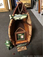 Photo of a fishing-themed lot featuring a woven basket shaped like a fish, a ceramic frog figurine with fishing pole, a shadow box with fishing lures, and a wooden base with small fishing collectibles.