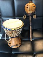 Photo of old mini drum and carved face rattle on black leather seat showing drum design and rattle facial features