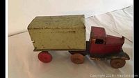Side view of vintage red covered tin toy truck with green cargo box and red wheels showing wear and patina
