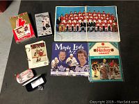 Photo of multiple hockey collectible items laid out on the floor: unopened Team Canada 1976 hockey card set, Team Canada large photo poster, NHL Player and Team Album, Maple Leafs book, and other hockey memorabilia.
