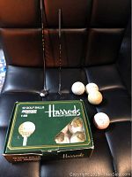 Photo showing box of Harrods Knightsbridge unopened golf balls, 4 vintage golf balls, and 2 mini golf clubs