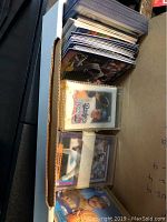 Large stack of baseball cards inside a cardboard box, some in plastic sleeves, showing various players and teams