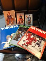 Vintage hockey programs and player photos displayed on a black leather chair, includes Toronto, Hartford, Detroit programs and goalie photos.
